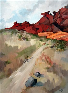 A hiking trail into the wash at Red Rock Canyon. Bright red and orange sandstone boulders peak over the top of the hill.