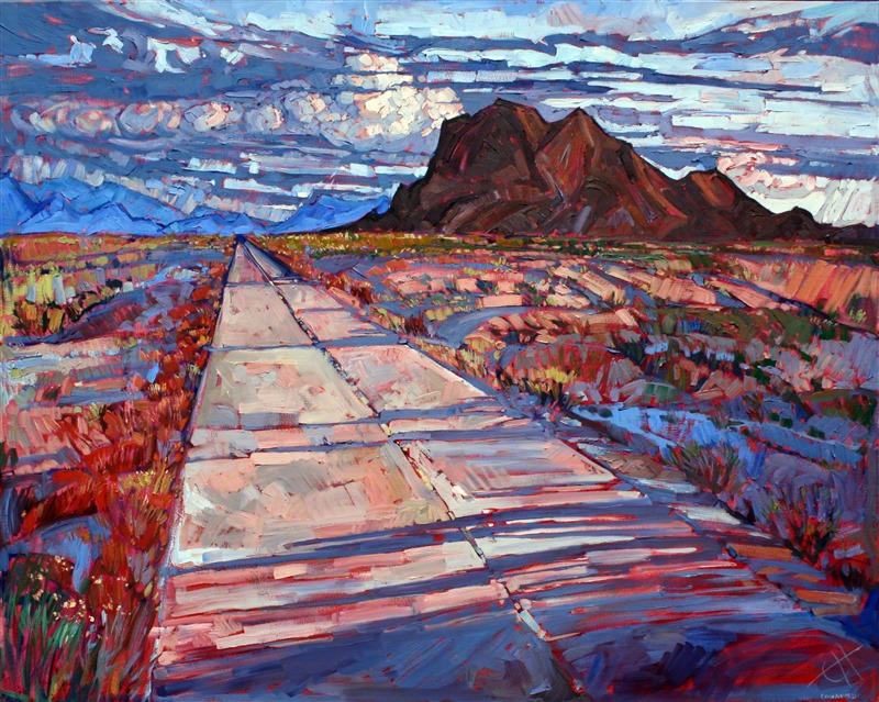 A straight desert highway moves towards the distant Arizona buttes, with long afternoon shadows crossing over the asphalt.