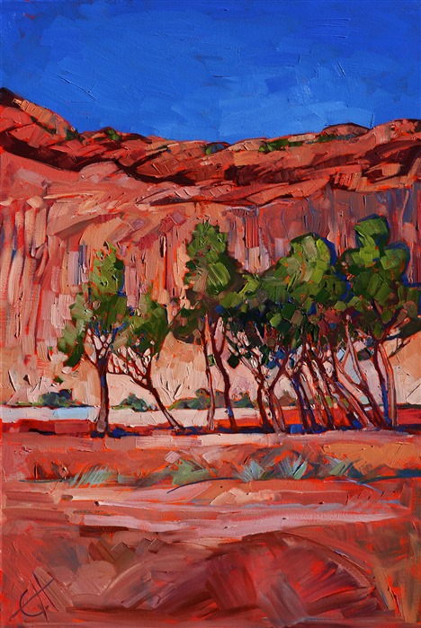 Summer green cottonwoods flank the red sandstone cliff side of Canyon de Chelly, Arizona. The canyon floor is wet with red mud, gently reflecting the landscape.