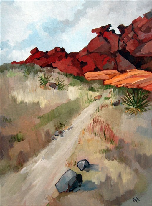 A hiking trail into the wash at Red Rock Canyon. Bright red and orange sandstone boulders peak over the top of the hill.